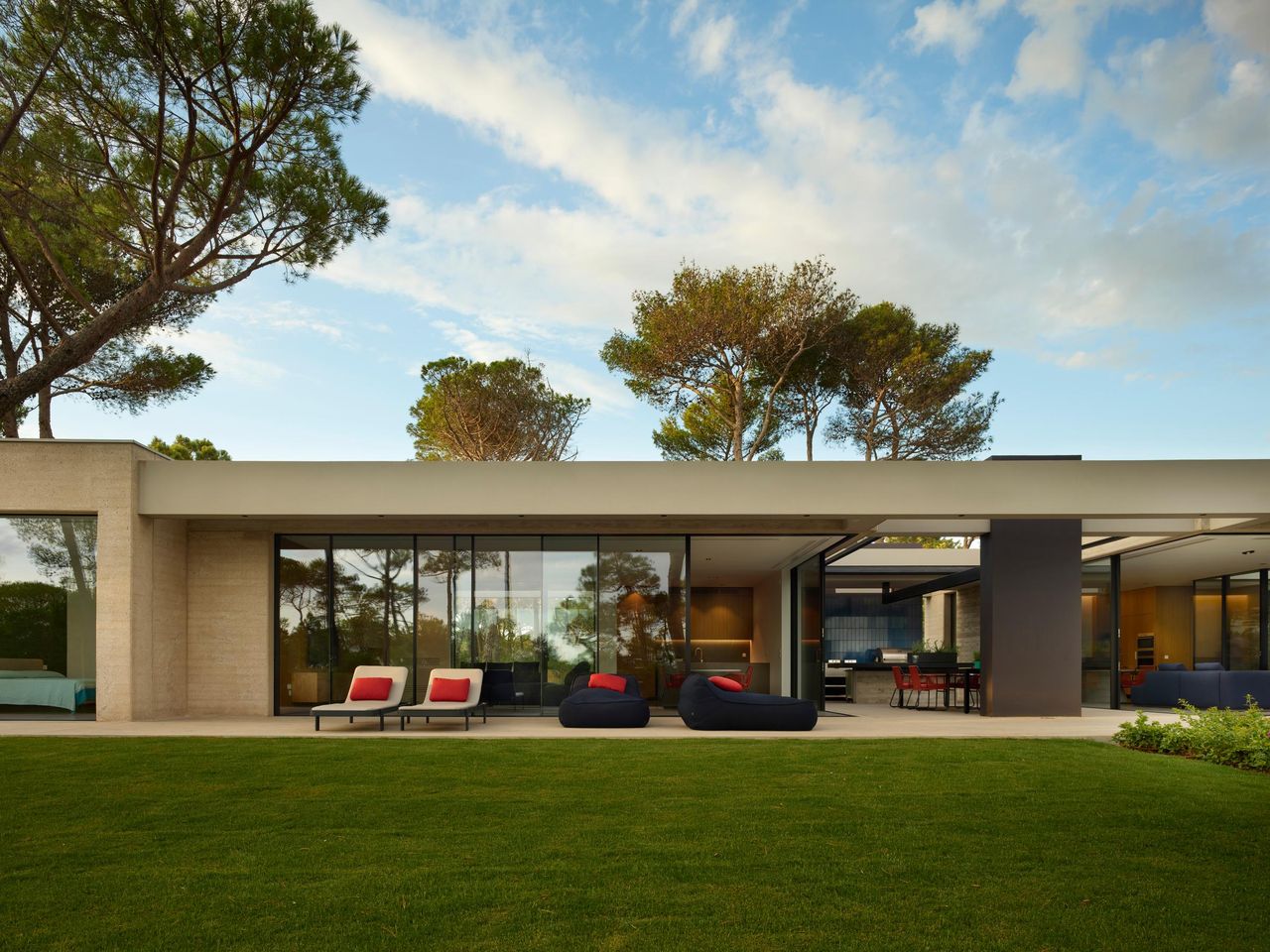 Long single-storey house under umbrella pines, its garden elevation glazed end to end with Sky-Frame