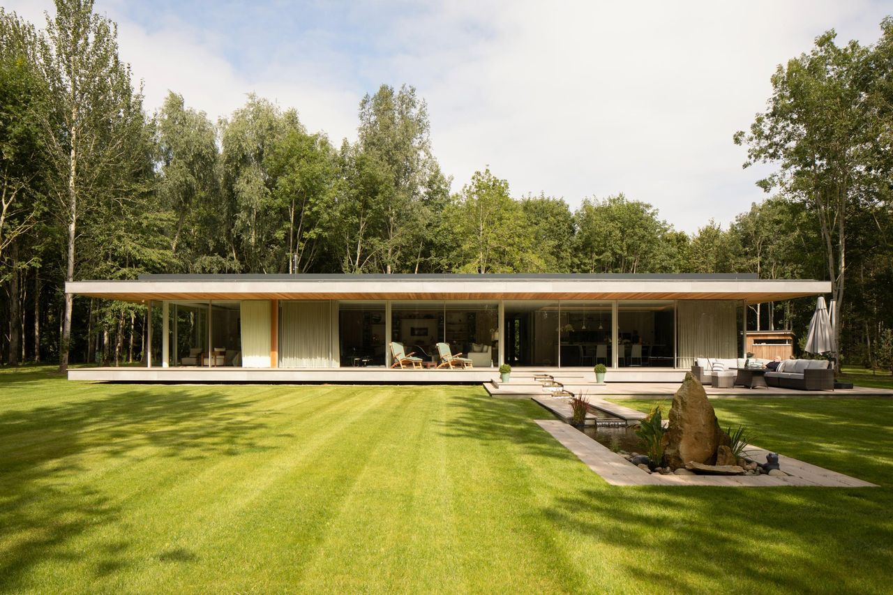 Single-storey pavilion across a lawn, its long elevation glazed with Sky-Frame against woodland