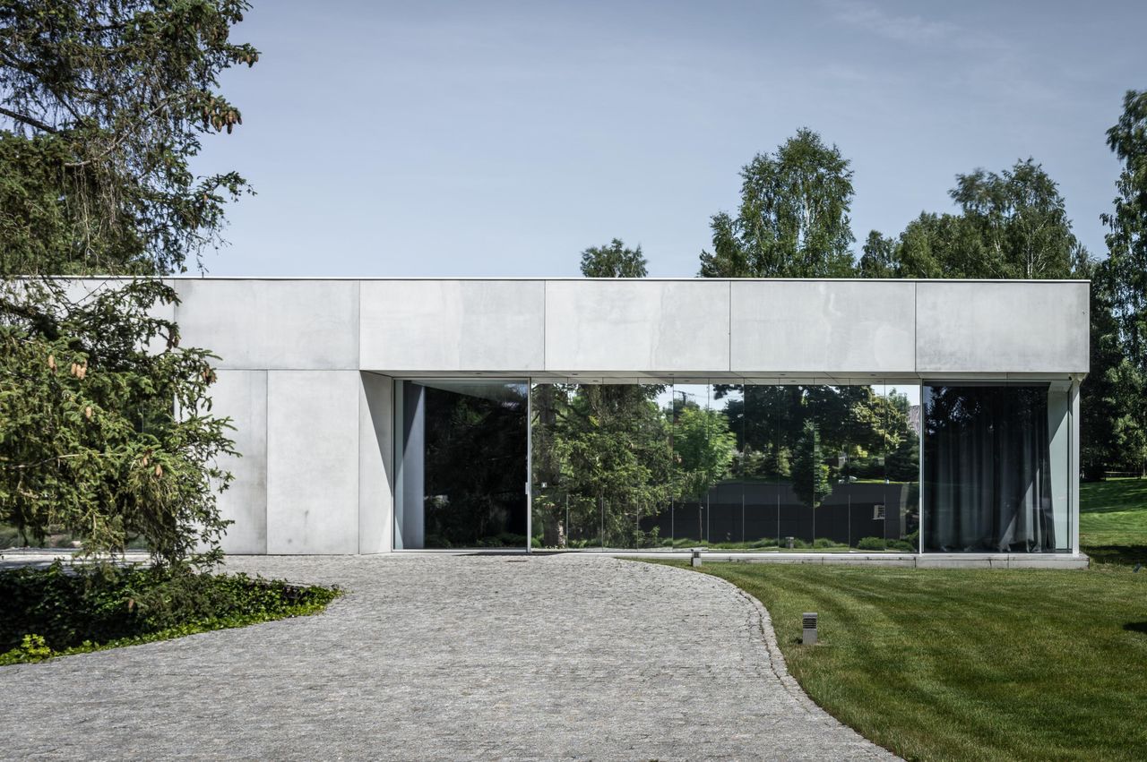 Single-storey concrete house behind a curving cobbled drive, its glazed front opened by a Sky-Frame Pivot door