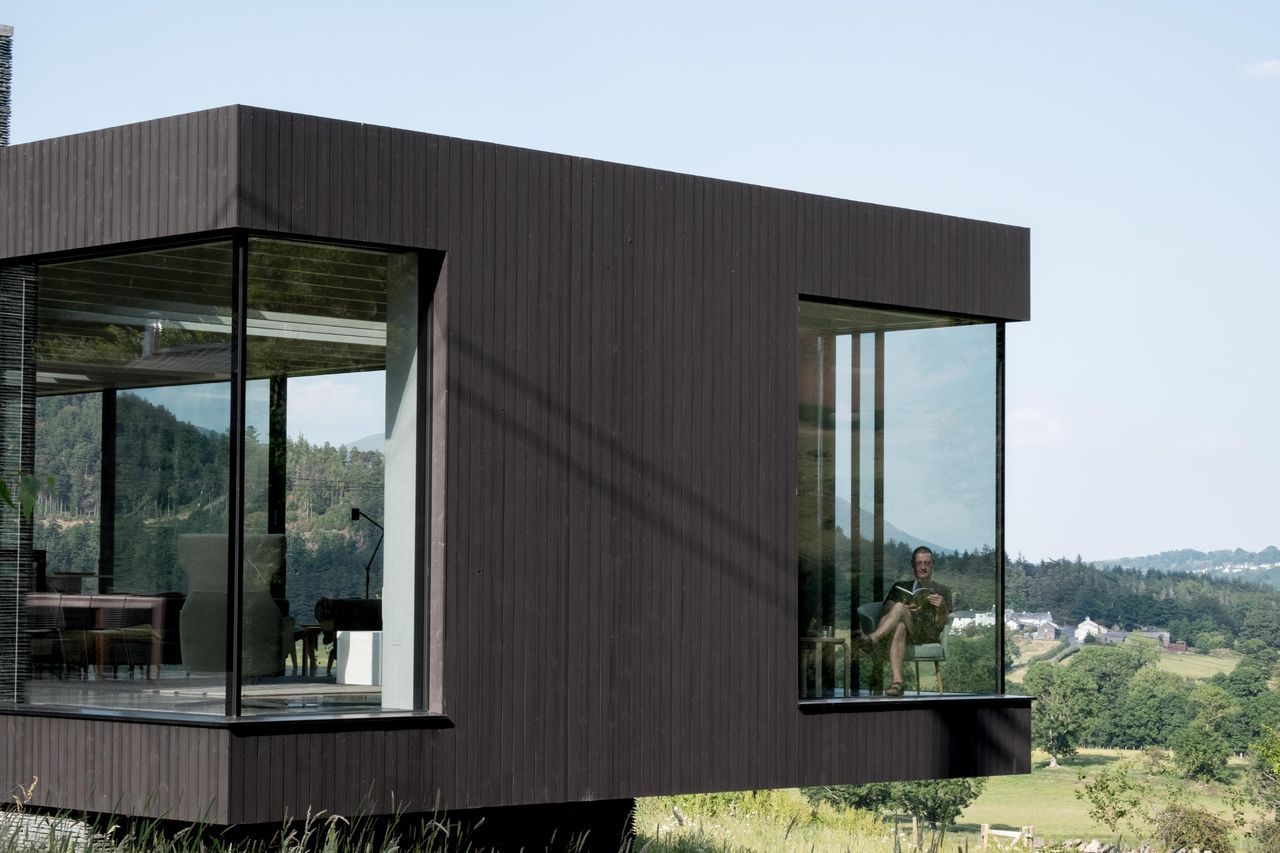 Dark-clad house cantilevered over a valley, with Sky-Frame glazing wrapping the corners