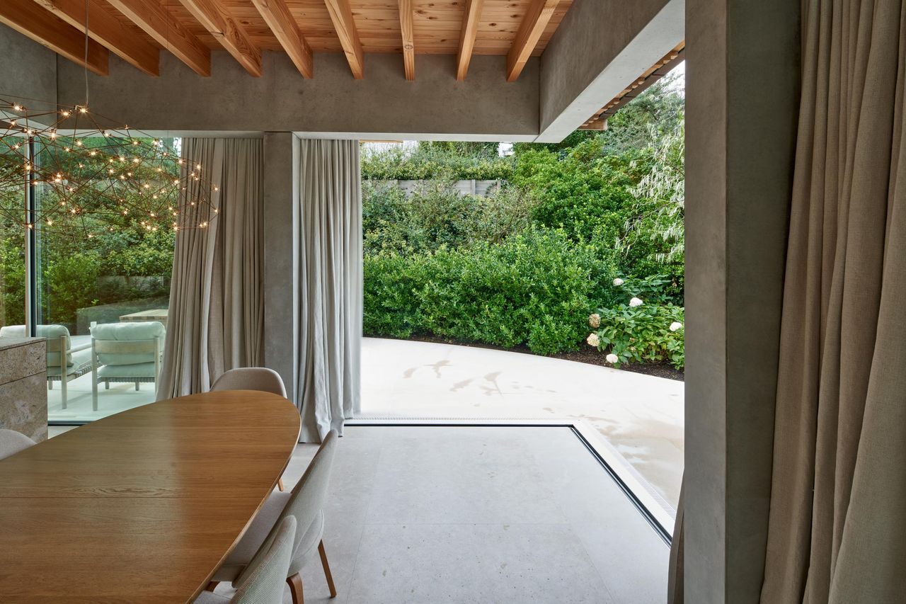 Dining space opening through a Sky-Frame sliding pane to a planted terrace, the track flush with the stone floor