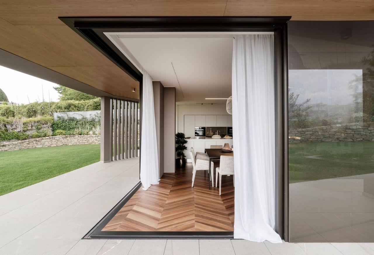 Corner of a house opened to the terrace, a Sky-Frame pane slid clear of the opening