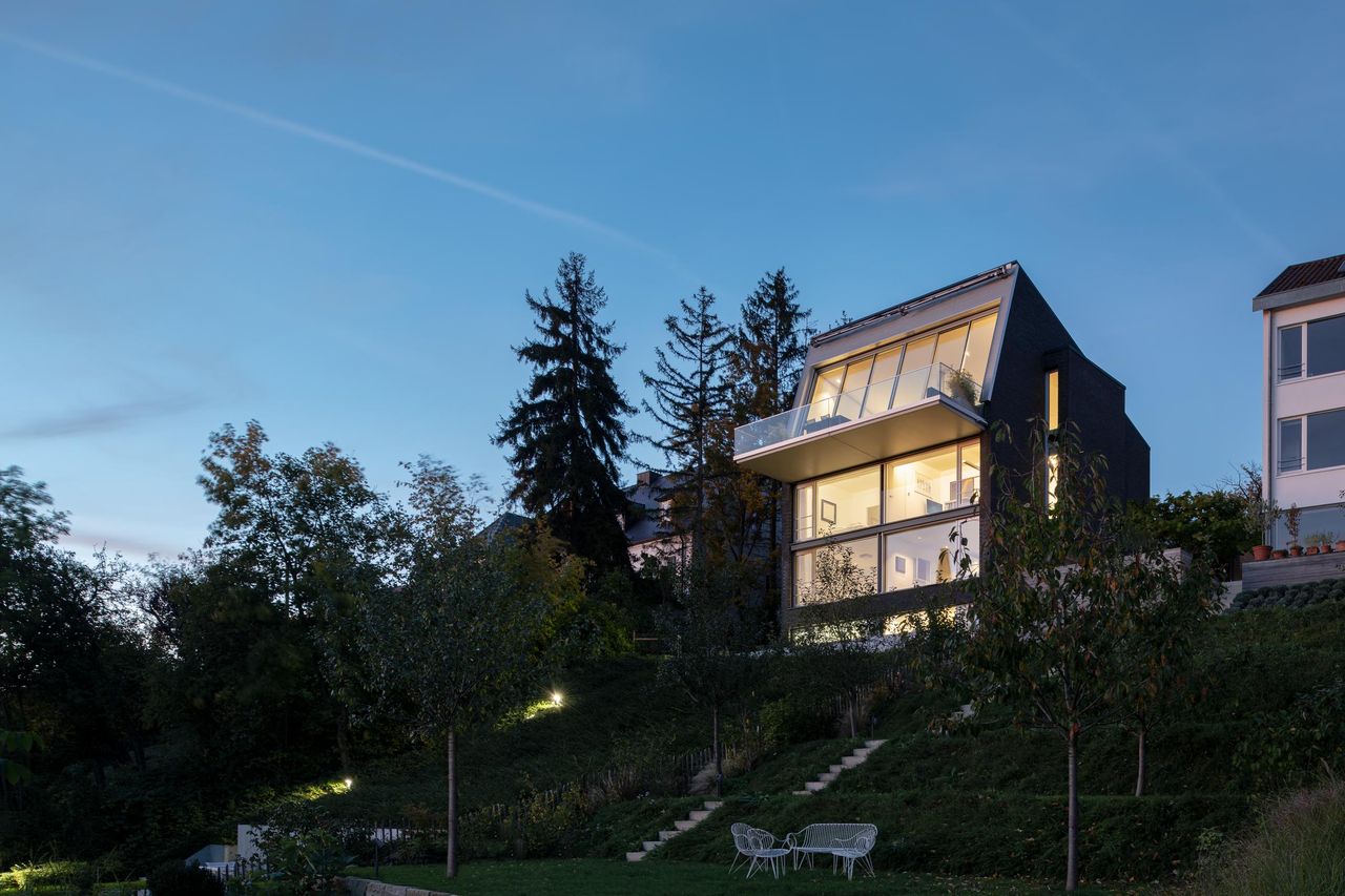 Hillside house at dusk, inclined Sky-Frame Slope glazing lit from within