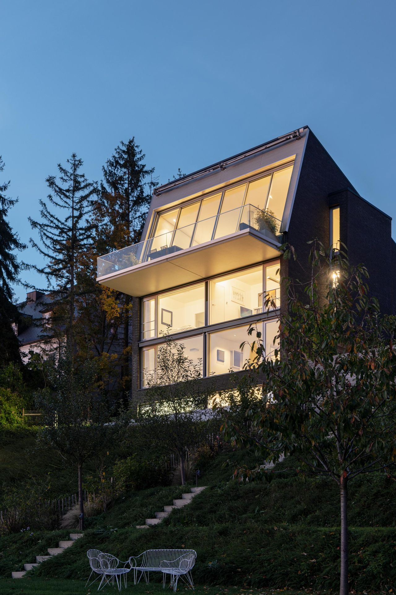 Hillside house at dusk with lit, inclined Sky-Frame Slope glazing above the garden terraces