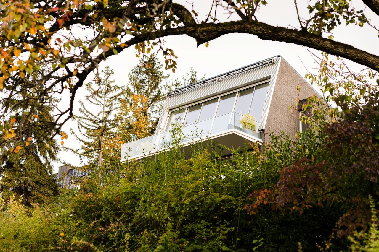 Hillside house among trees, its upper floor glazed with inclined Sky-Frame Slope panes